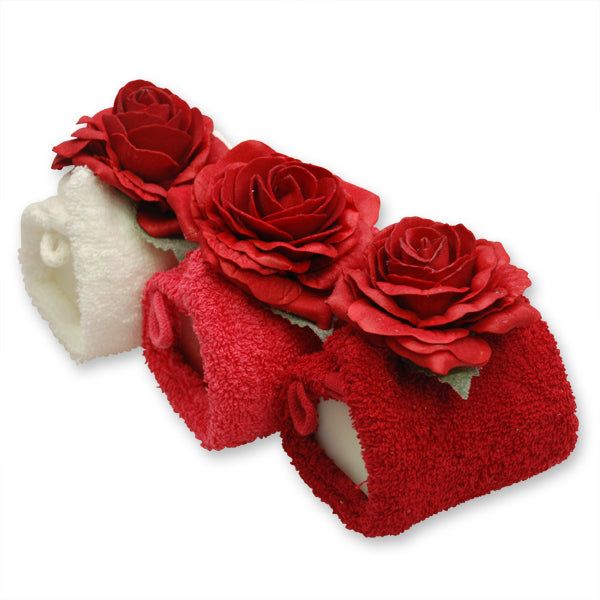 Drei Schafmilchseifen in Waschlappen, dekoriert mit roten Rosen. Eine weiße, zwei rote. Eckige Form.