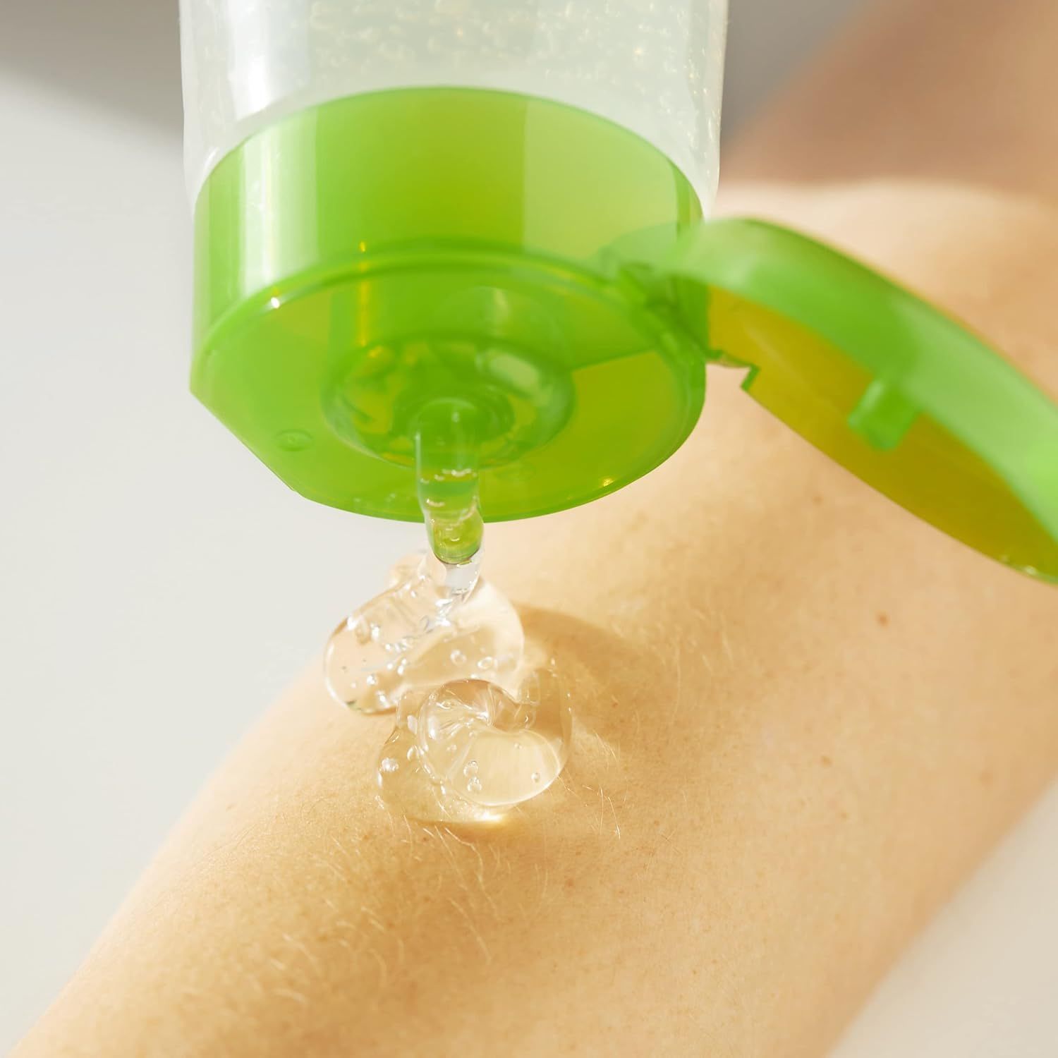 Grüner Deckel einer Tube, Gel wird auf die Haut gedrückt. Transparentes Gel kommt heraus.