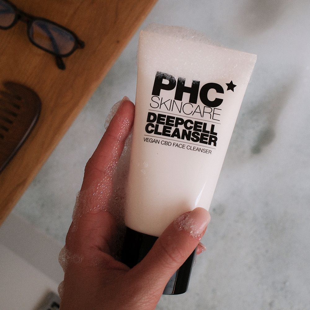 Weiße Tube mit schwarzem Deckel. Aufschrift: PHC Skincare Deepcell Cleanser. Wird von einer Hand gehalten.