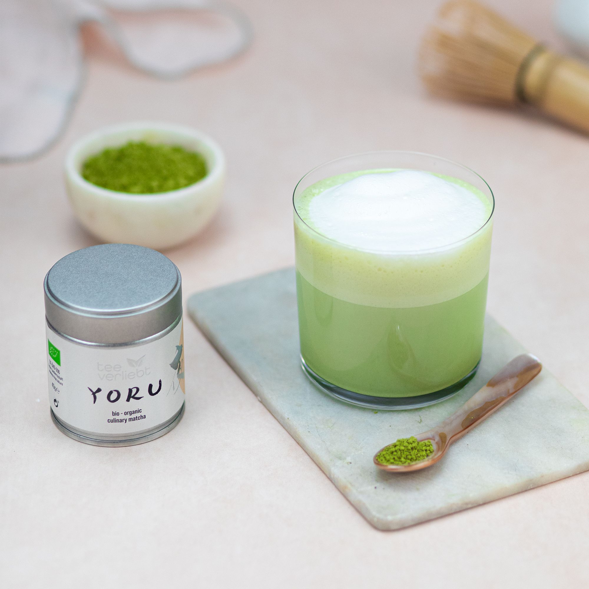 Glas Matcha-Getränk, Dose Yoru, Schale und Löffel mit Matcha. Schneebesen. Auf Marmorplatte. Hintergrund unscharf.