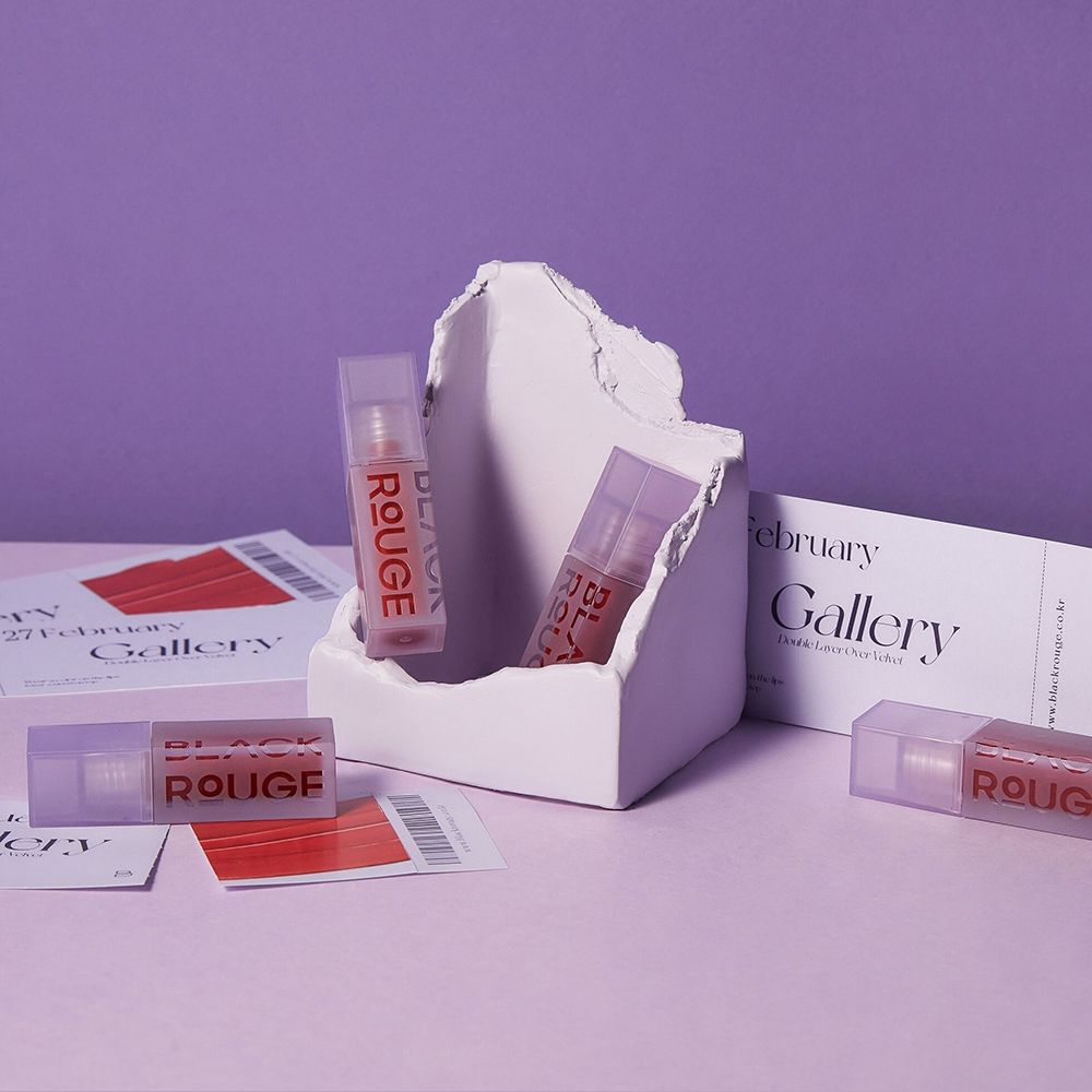 Mehrere Lipgloss-Fläschchen in einer weißen Skulptur. Auf lila Untergrund. Etiketten und Karten liegen daneben.