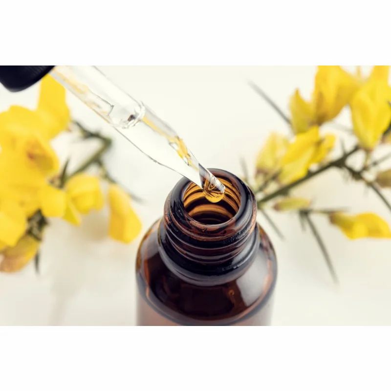 Braune Glasflasche mit Pipette. Öl wird in die Flasche getropft. Gelbe Blüten im Hintergrund.
