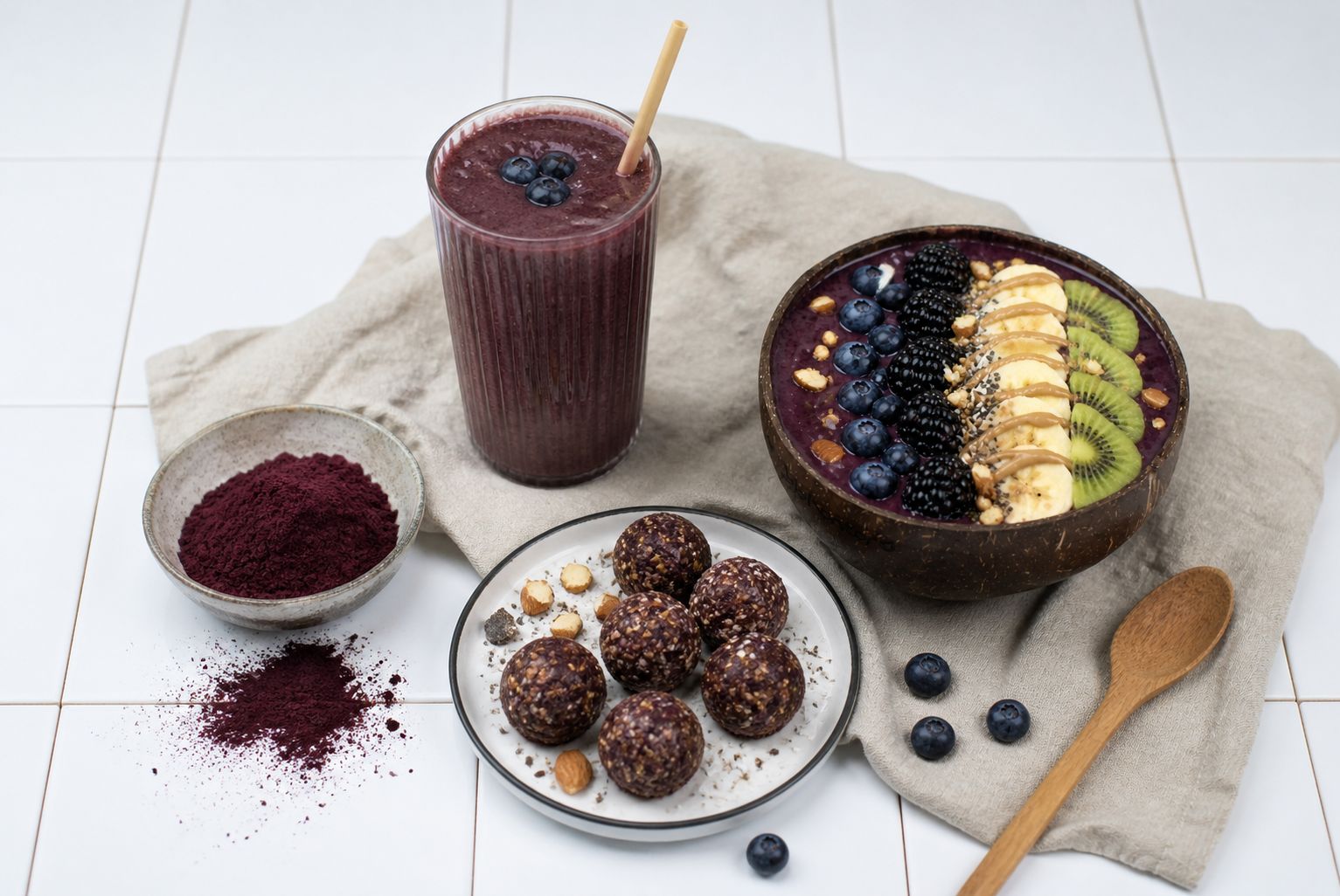 Açaí Schale mit Früchten, ein Glas Smoothie, Schale mit Energiebällchen und Açaí Pulver.