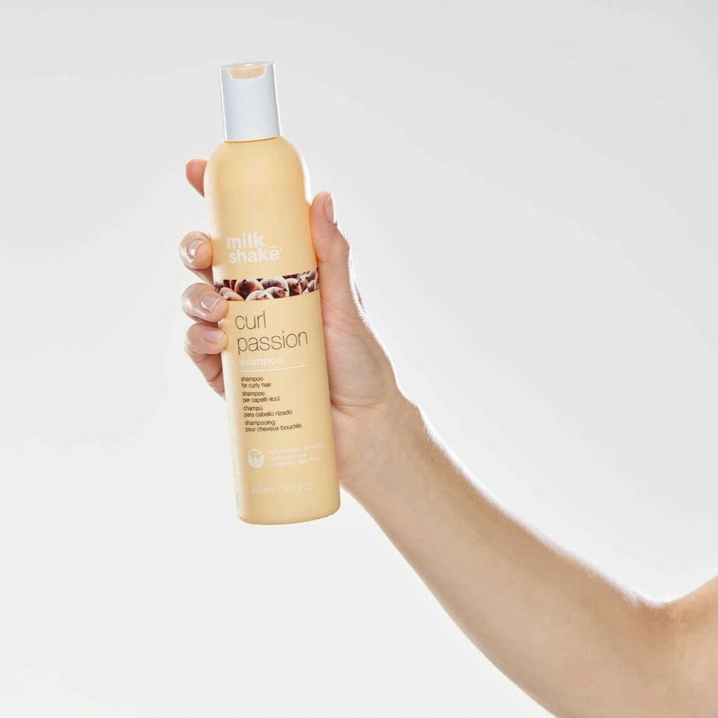 Hand hält eine beigefarbene Shampoo-Flasche mit weißem Deckel. Aufschrift: milk_shake, curl passion shampoo. Für lockiges Haar.