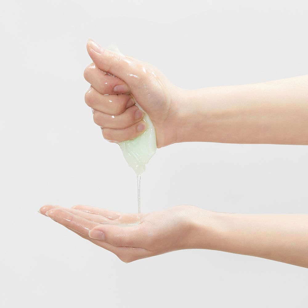 Hände halten eine grüne, gelartige Substanz. Flüssigkeit tropft in eine Hand. Helle Haut.