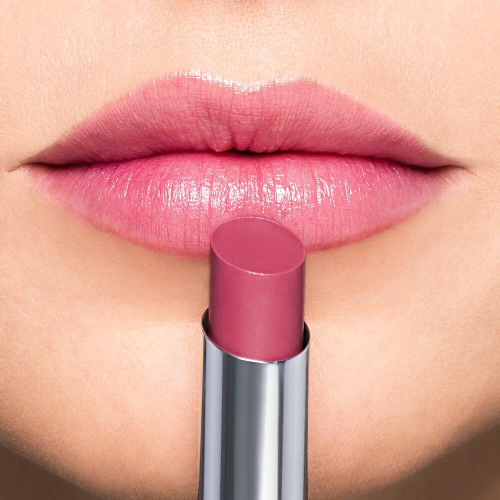 Nahaufnahme von Lippen, auf die ein rosafarbener Lippenbalsam aufgetragen wird.