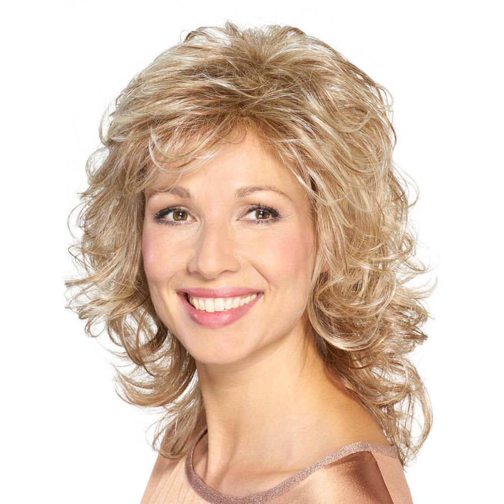 Frau mit blond gelockter Perücke. Die Perücke hat einen Pony und ist leicht gestuft. Sie trägt ein helles Oberteil.