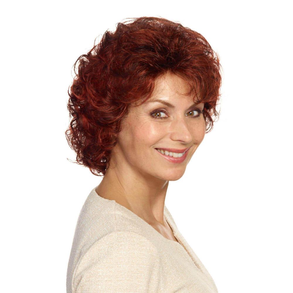 Frau mit roter, lockiger Perücke. Sie trägt ein cremefarbenes Oberteil und lächelt in die Kamera.