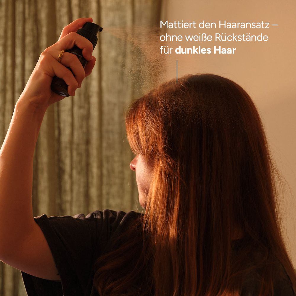 Person sprüht Trockenshampoo auf dunkelbraunes Haar. Text: Mattiert den Haaransatz – ohne weiße Rückstände für dunkles Haar.