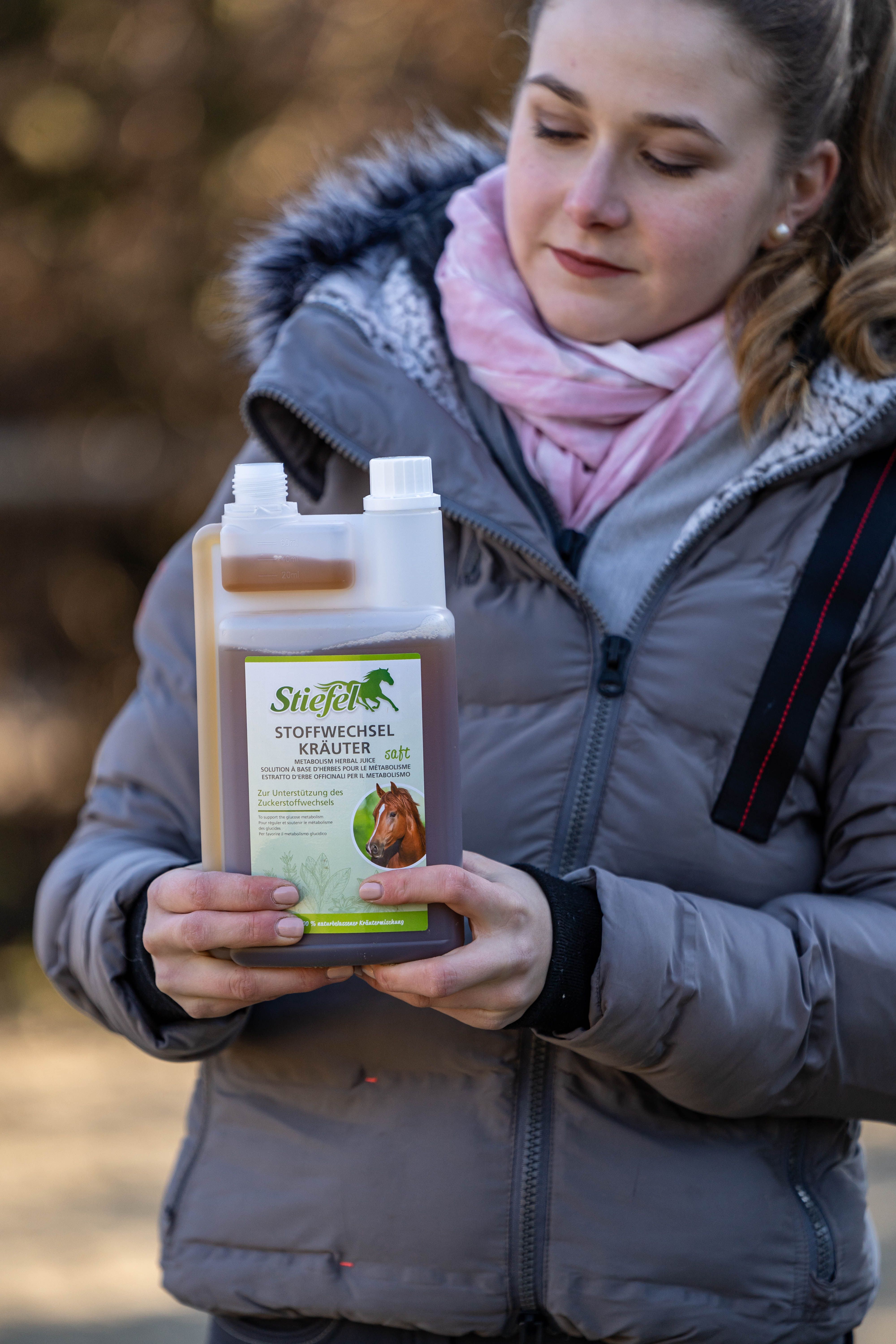 Frau hält eine Flasche Stiefel Stoffwechselkräuter. Die Flasche hat einen weißen Deckel und ein grünes Etikett mit einem Pferd.