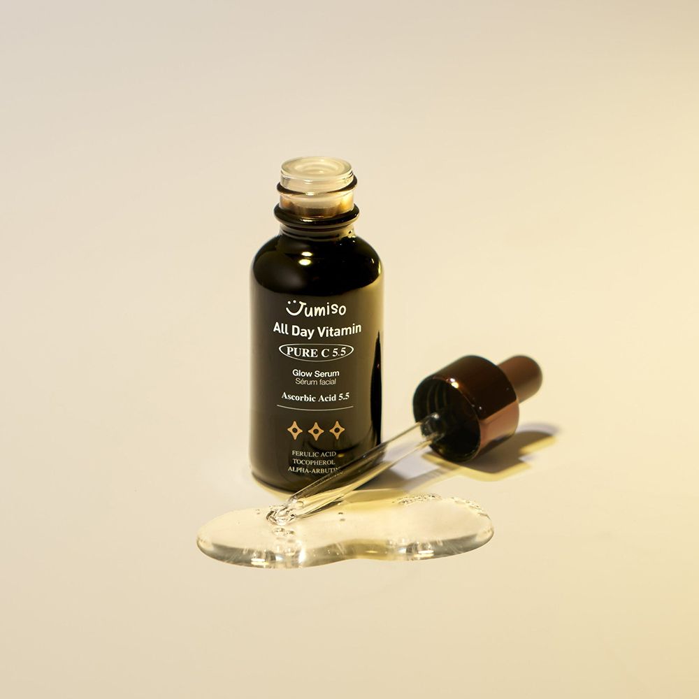 Dunkle Glasflasche mit braunem Deckel und Pipette. Daneben Serum-Tropfen. Aufschrift: JUMISO All Day Vitamin Pure C 5.5 Glow Serum.