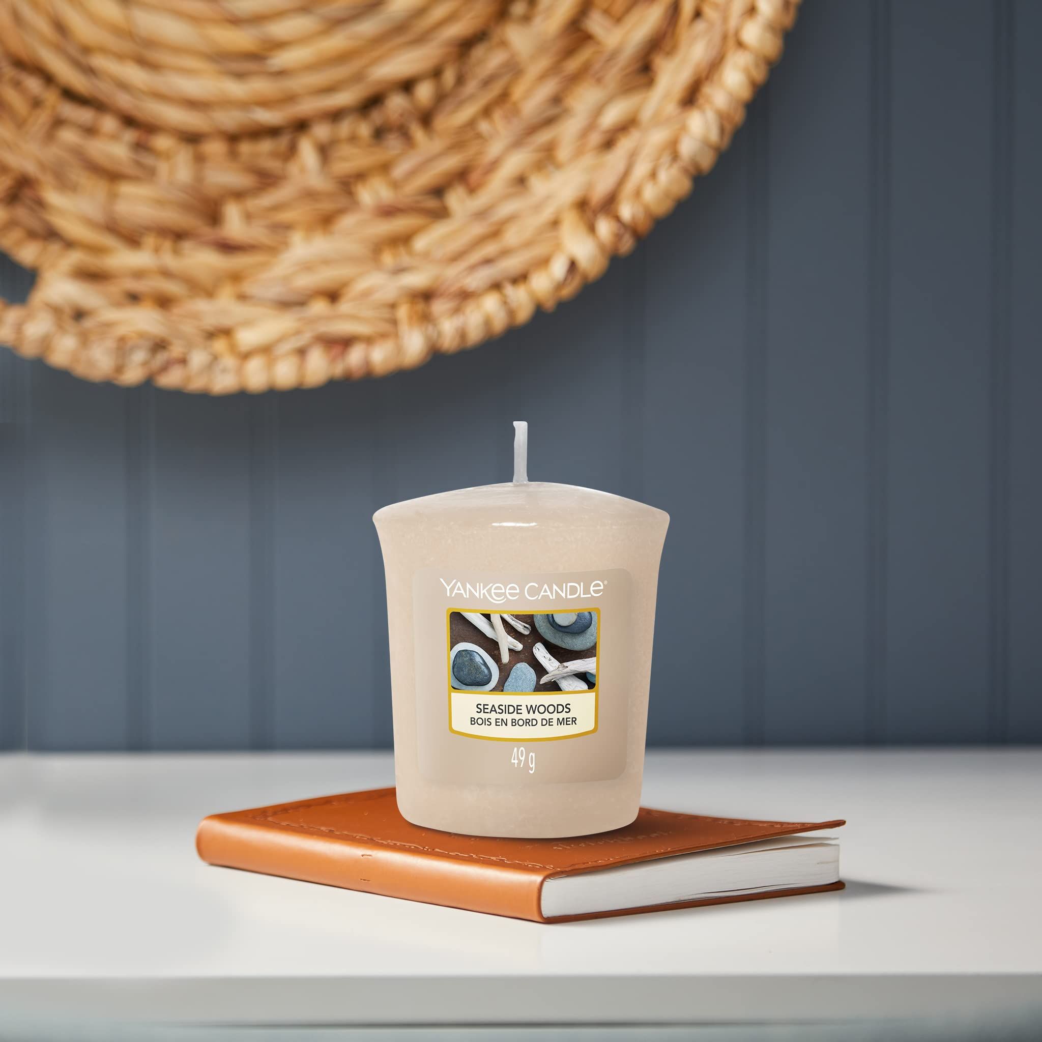 Beige Kerze auf Buch. Aufschrift: Yankee Candle, Seaside Woods, 49g. Korb im Hintergrund.