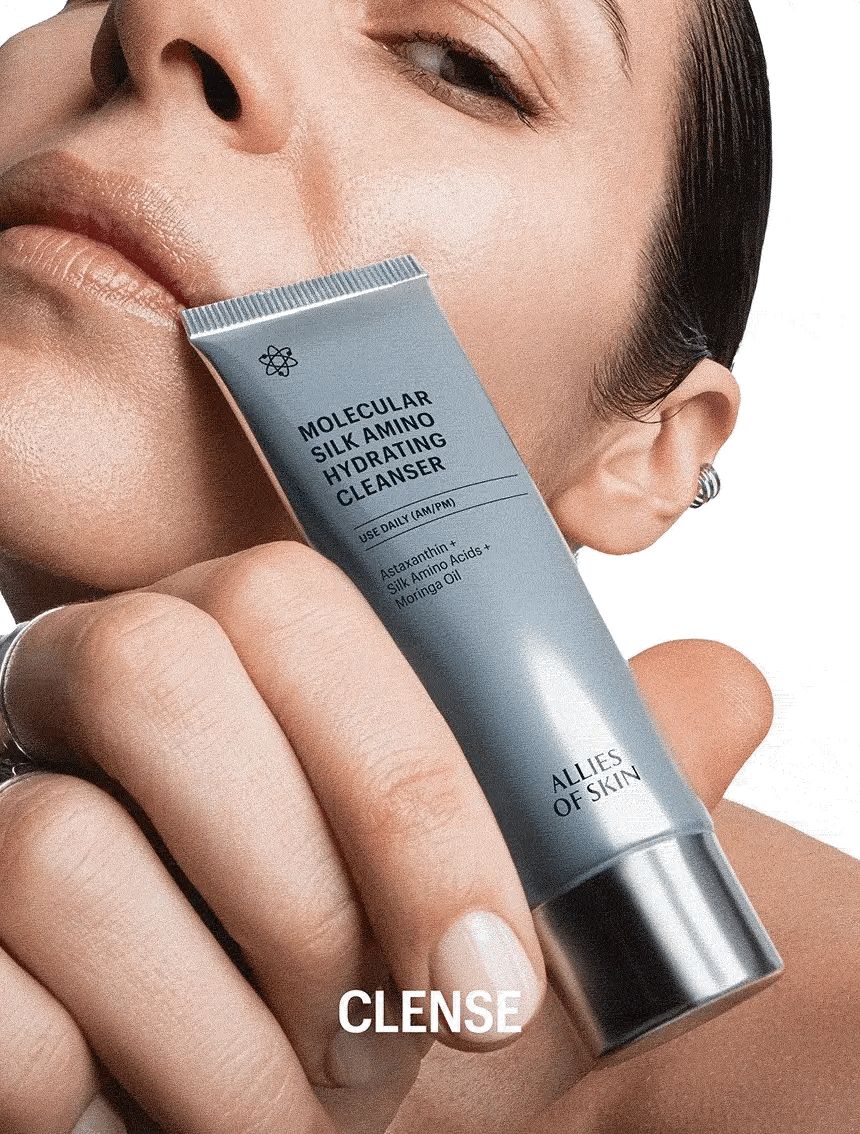 Person hält eine Tube. Aufschrift: Molecular Silk Amino Hydrating Cleanser. Marke: ALLIES OF SKIN. Text: CLENSE.