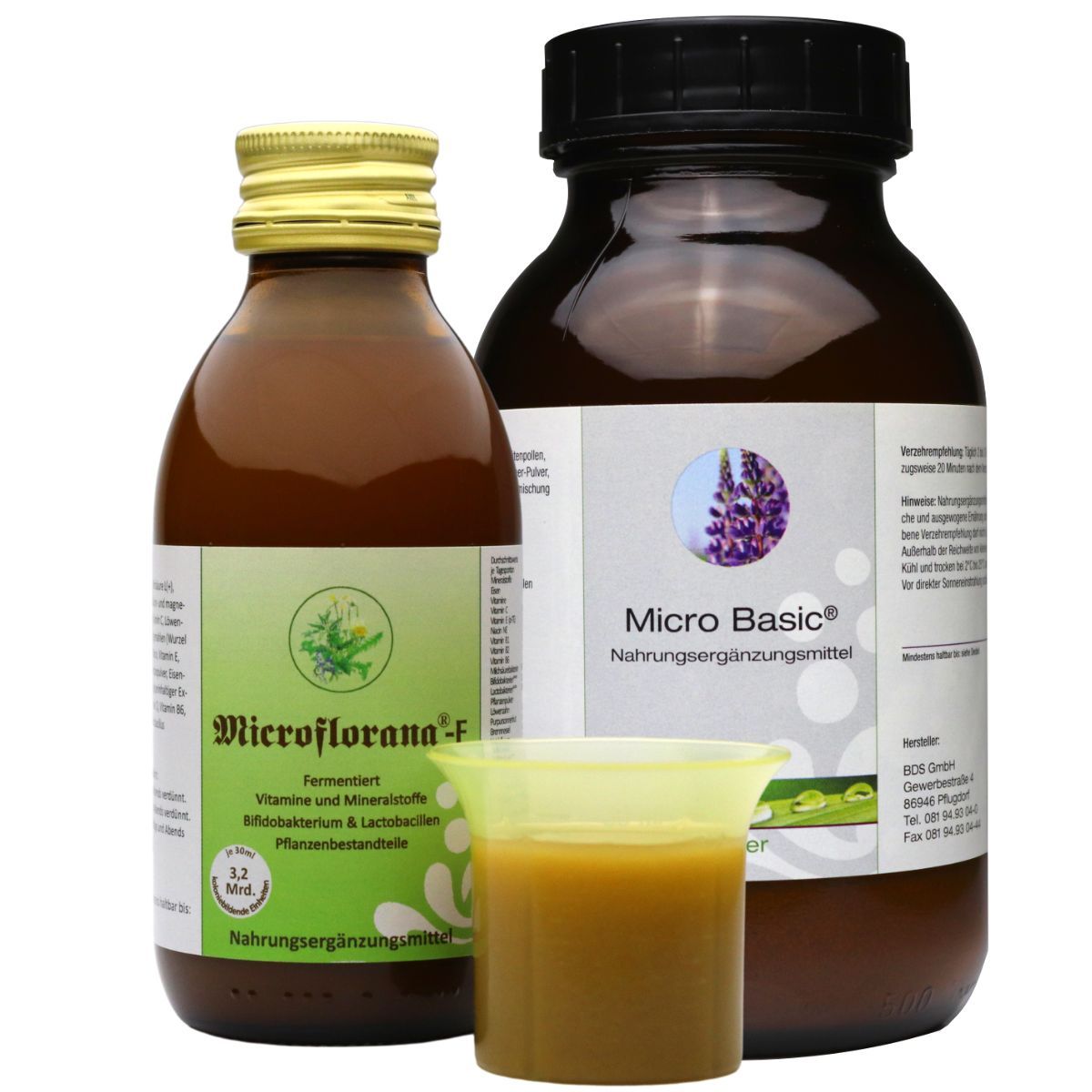 Zwei braune Glasflaschen mit Etiketten, ein Messbecher mit Flüssigkeit. Aufschrift: Microflorana-F, Micro Basic.