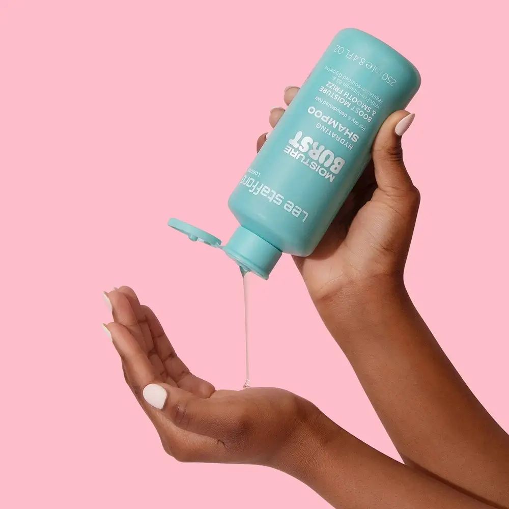Hände halten türkisfarbene Shampoo-Flasche. Shampoo fließt heraus. Aufschrift: Moisture Burst Hydrating Shampoo.