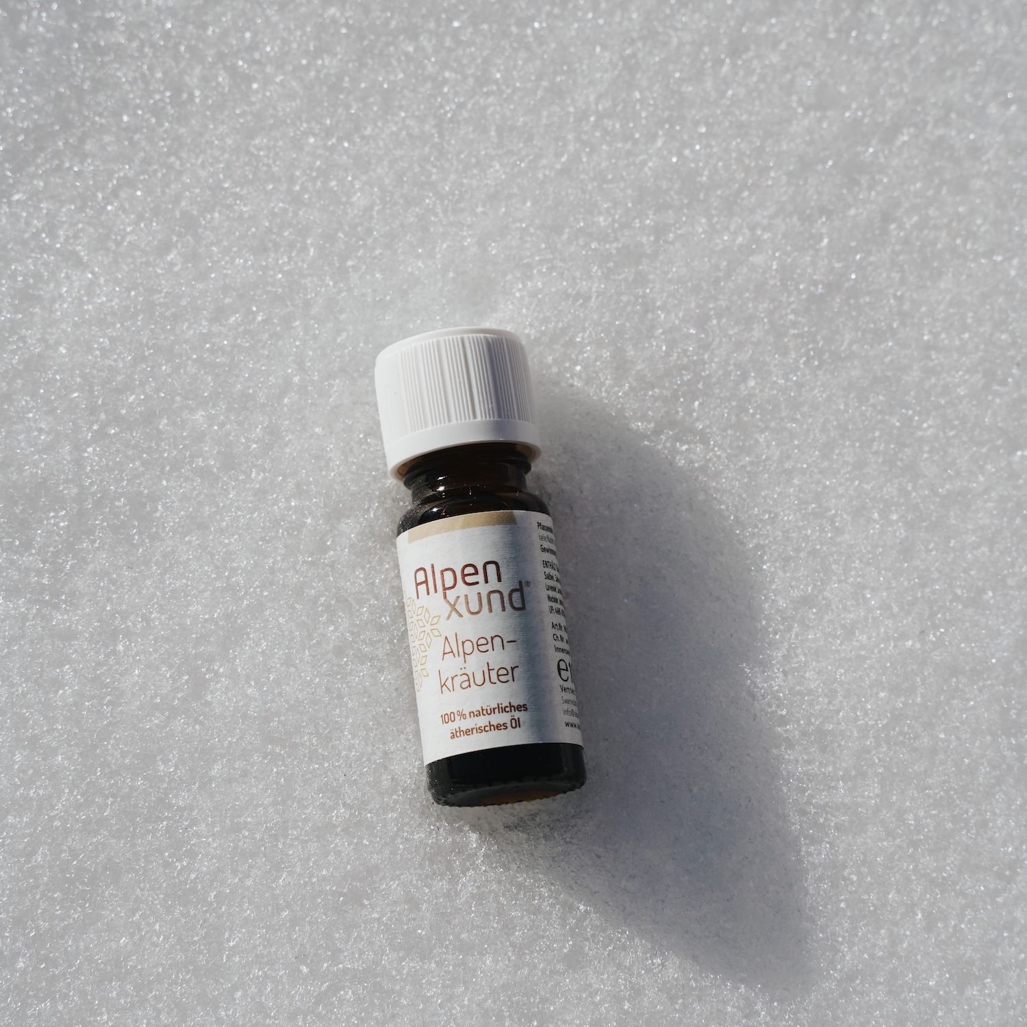 Braune Glasflasche mit weißem Deckel auf weißem Untergrund. Beschriftung: Alpenxund Alpenkräuter ätherisches Öl.