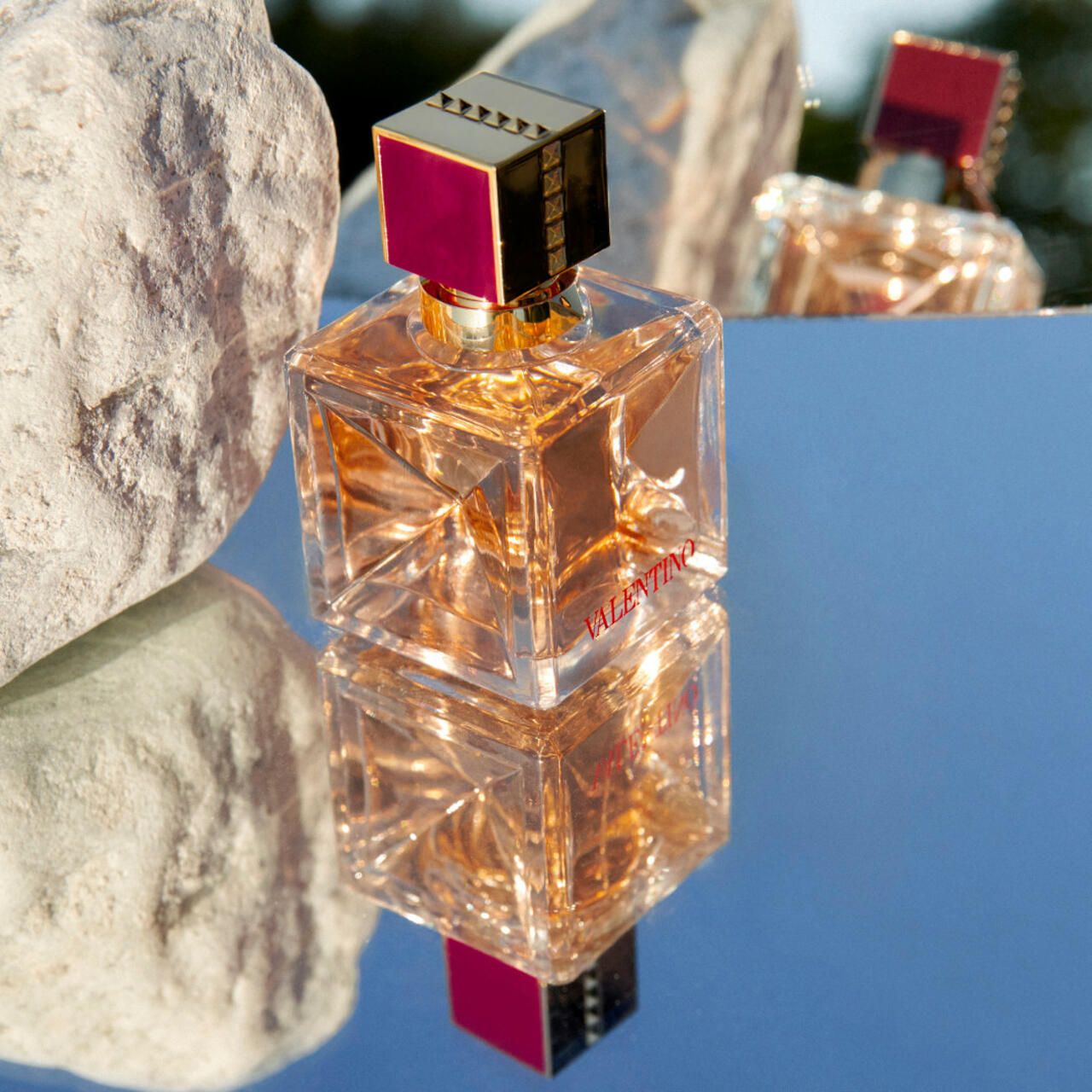 Parfümflakon auf spiegelnder Oberfläche. Flakon quadratisch, goldener Verschluss. Aufschrift: VALENTINO.