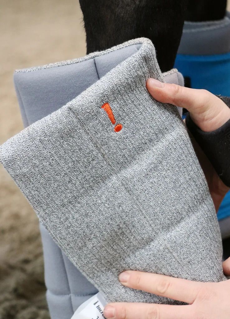 Graues Pad mit orangefarbenem Logo. Das Pad wird von einer Person gehalten, die es an einem Bein platziert.