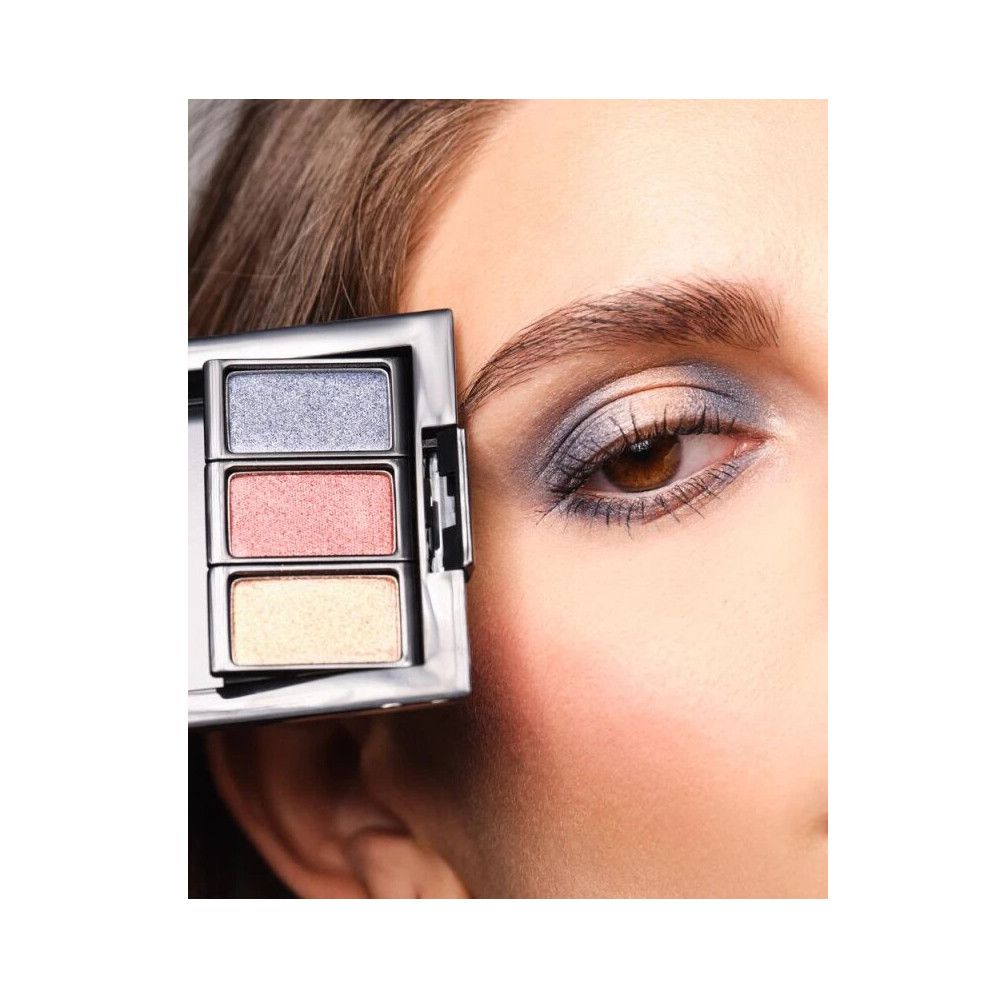 Eine Palette mit drei Lidschattenfarben. Das Produkt wird neben einem Auge gehalten, auf dem die Farben aufgetragen wurden.