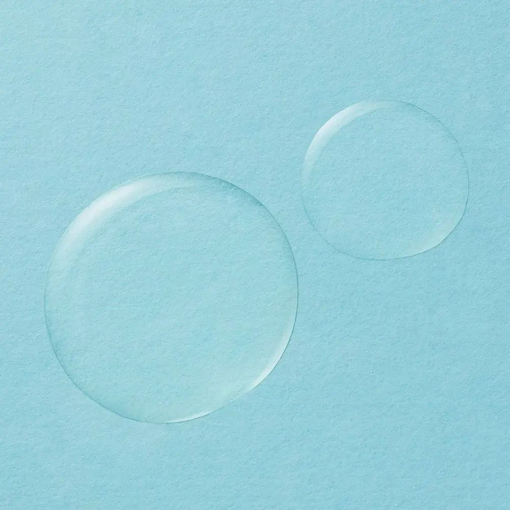 Zwei Tropfen Körperöl auf hellblauem Hintergrund. Runde Form, transparente Flüssigkeit.