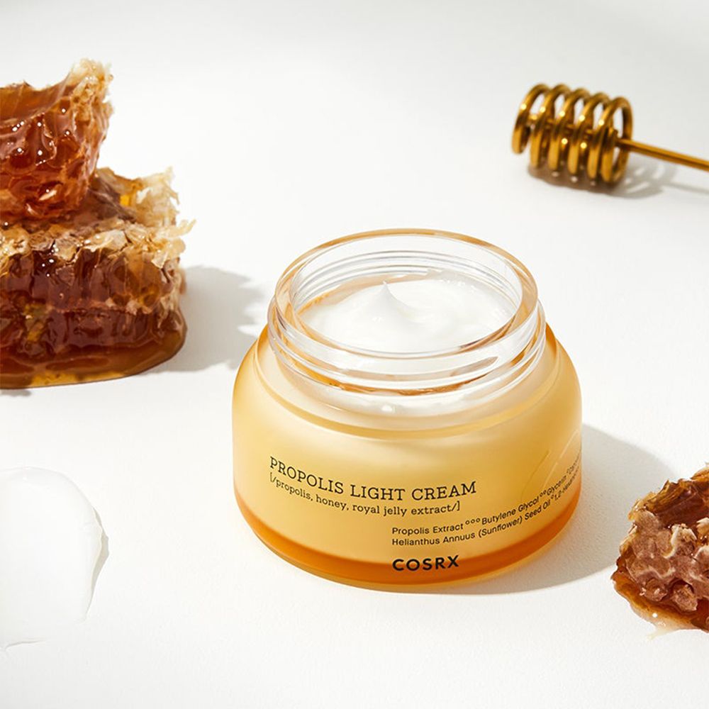 COSRX Propolis Light Cream in einem Glasbehälter mit Honigwaben und Honigrührer.