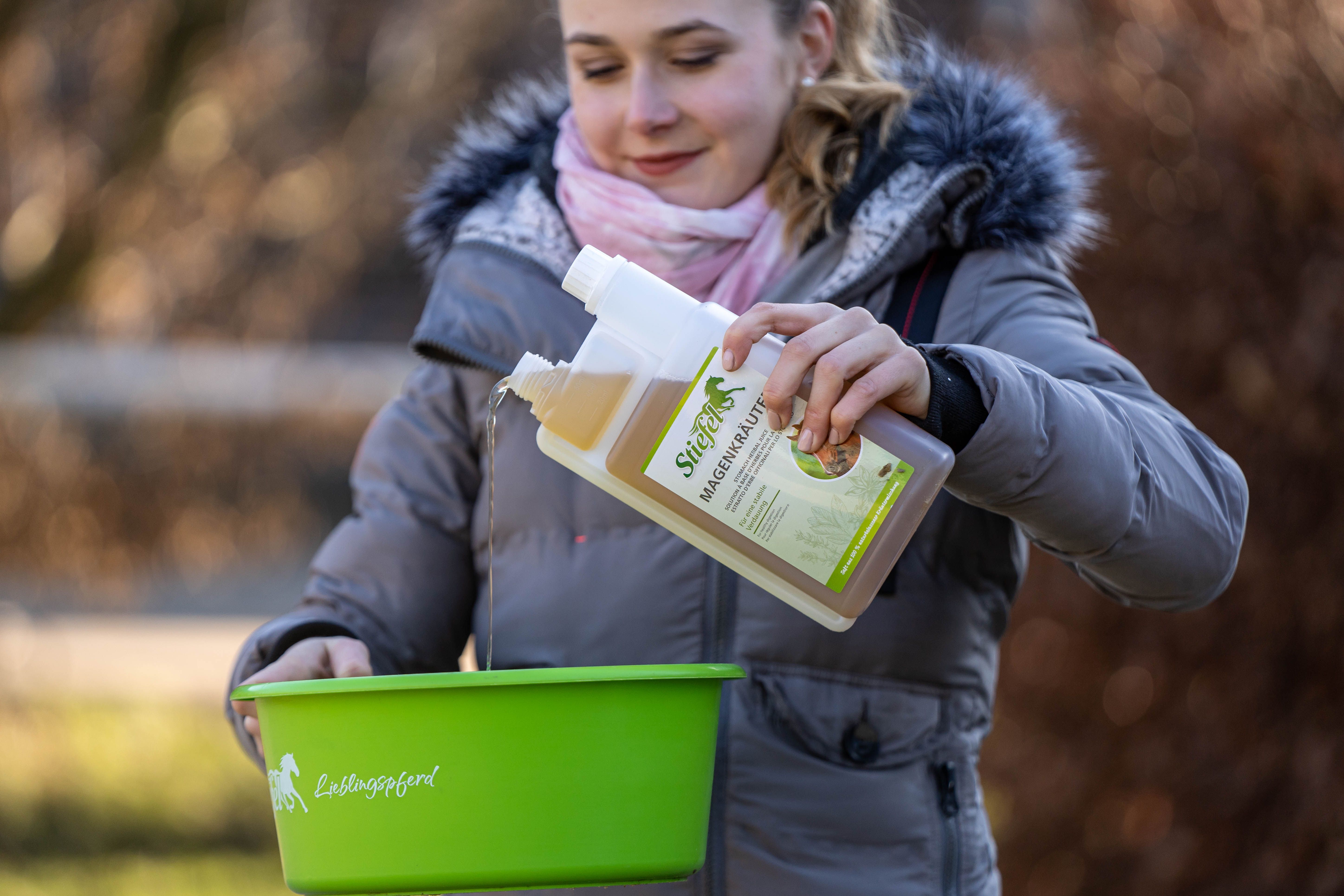Person gießt Kräutersaft in eine grüne Wanne. Flasche mit Produktnamen und Logo. Flasche mit zwei Kammern.