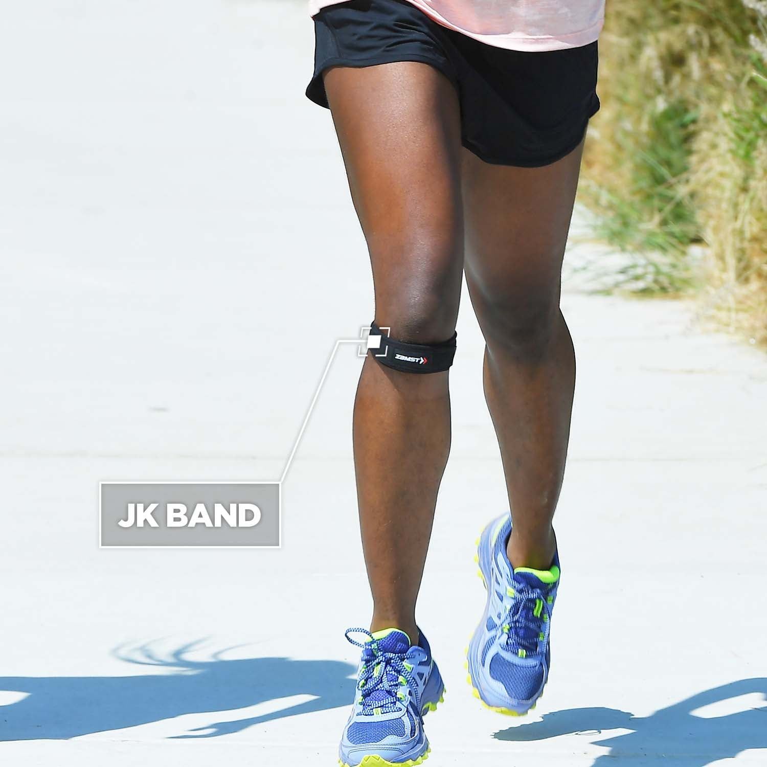 Läuferin mit JK Band am Knie. Schwarzes Band, Text JK BAND. Person trägt Laufschuhe.