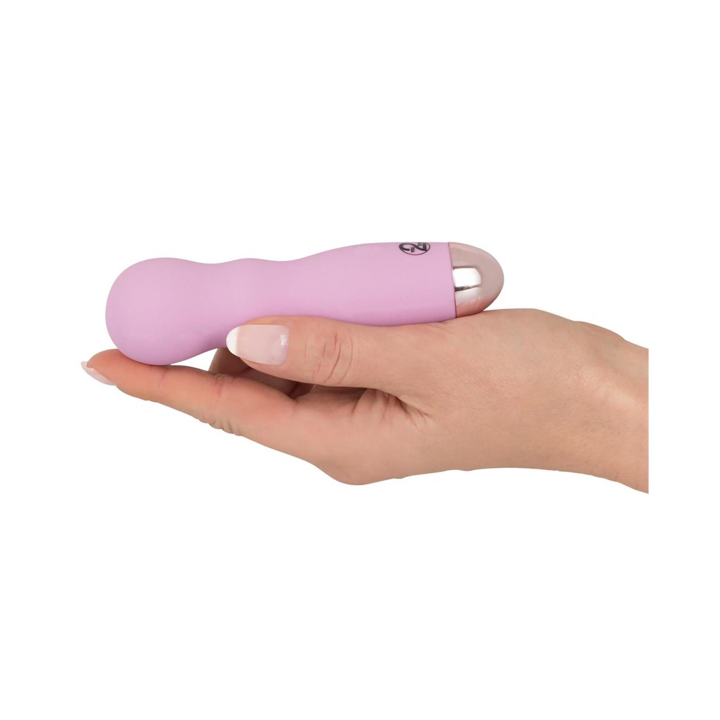 Mini-Vibrator in Hand gehalten. Rosa, zylindrisch, silberfarbene Spitze. Wellenförmiger Griff.