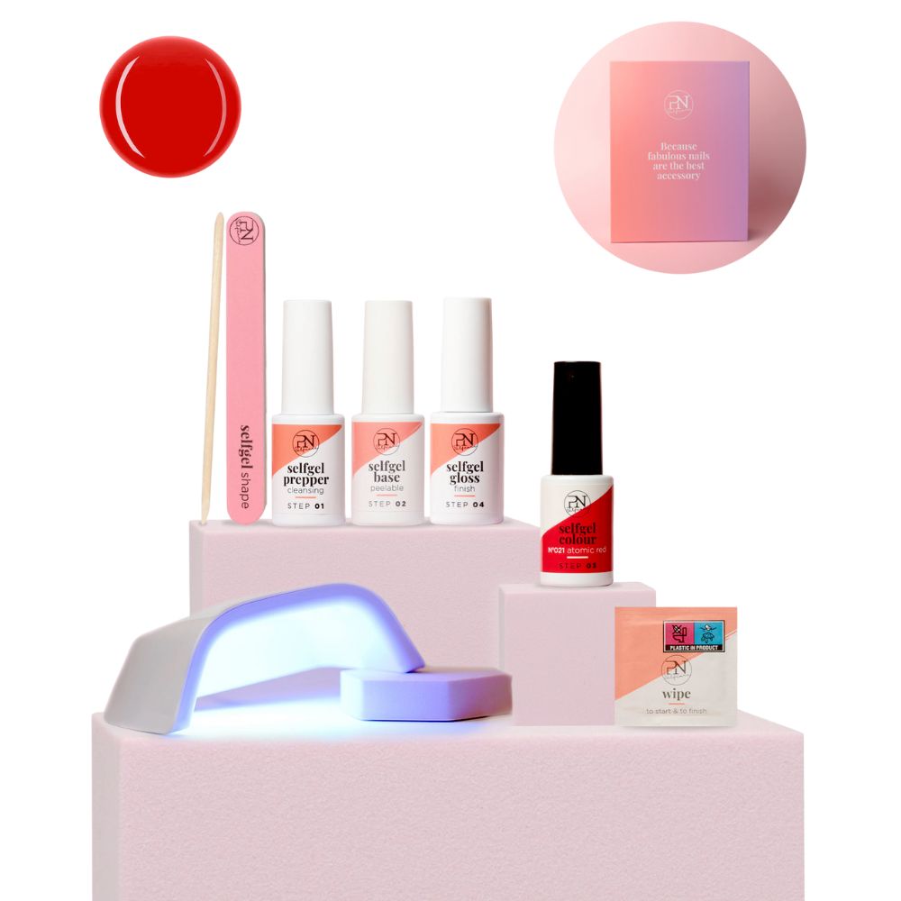 PN Selfcare Kit. Rotes Gel, Feile, 3 Flaschen, LED-Lampe, Reinigungstücher. Auf rosa Podest. Produktverpackung im Hintergrund.