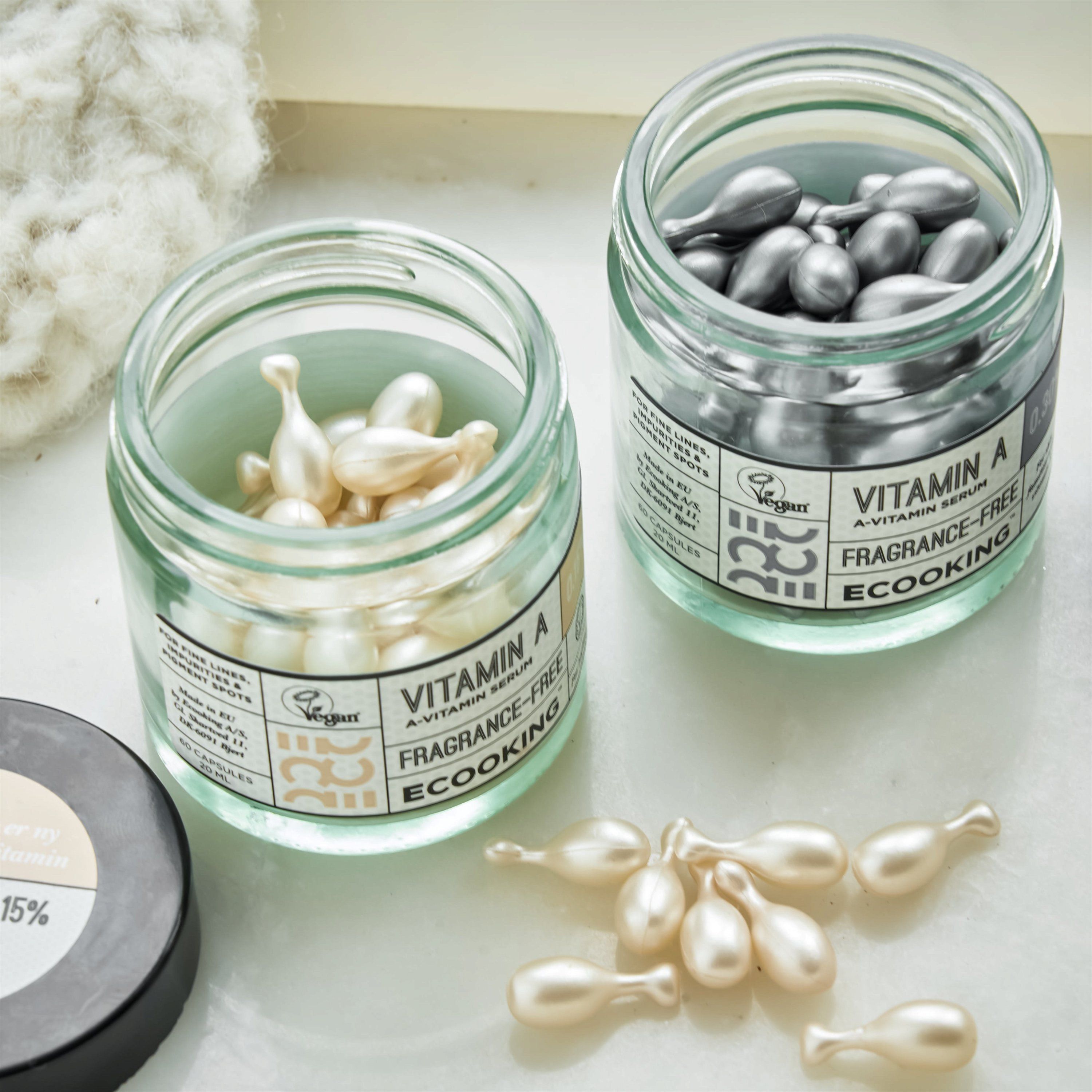 Zwei Gläser mit Kapseln. Aufschrift: Vitamin A 0,30%, Fragrance-Free, Ecooking. Vegan-Siegel. Kapseln daneben.