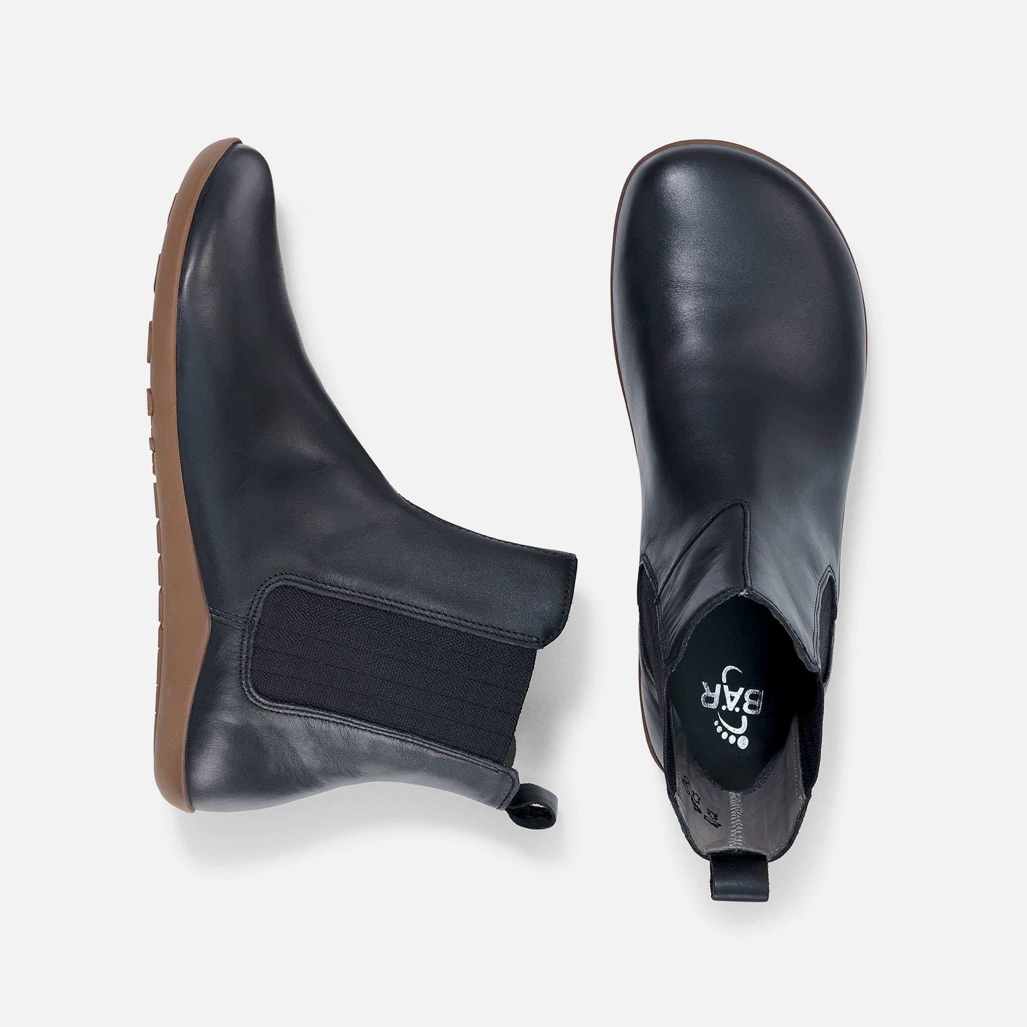 Zwei schwarze Stiefeletten, flache Sohle, breite Passform. Elastischer Einsatz an der Seite. Blick von oben.