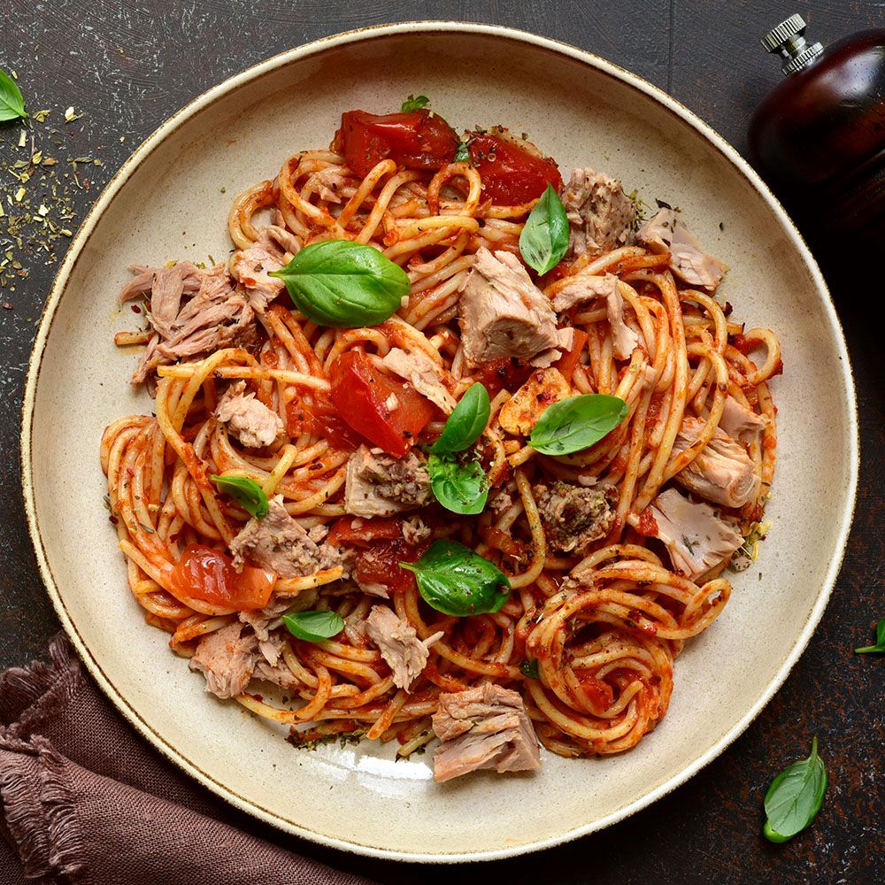 Teller mit Spaghetti, Tomaten, Thunfisch und Basilikum. Draufsicht. Dunkler Hintergrund. Pfeffermühle.