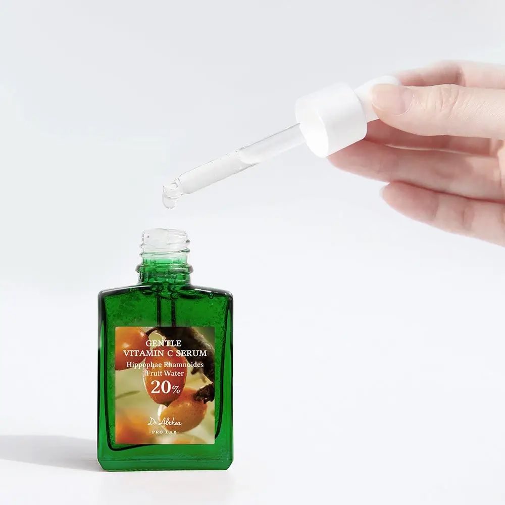 Grüne Glasflasche mit Pipette. Hand hält Pipette über offener Flasche. Aufschrift: Gentle Vitamin C Serum.