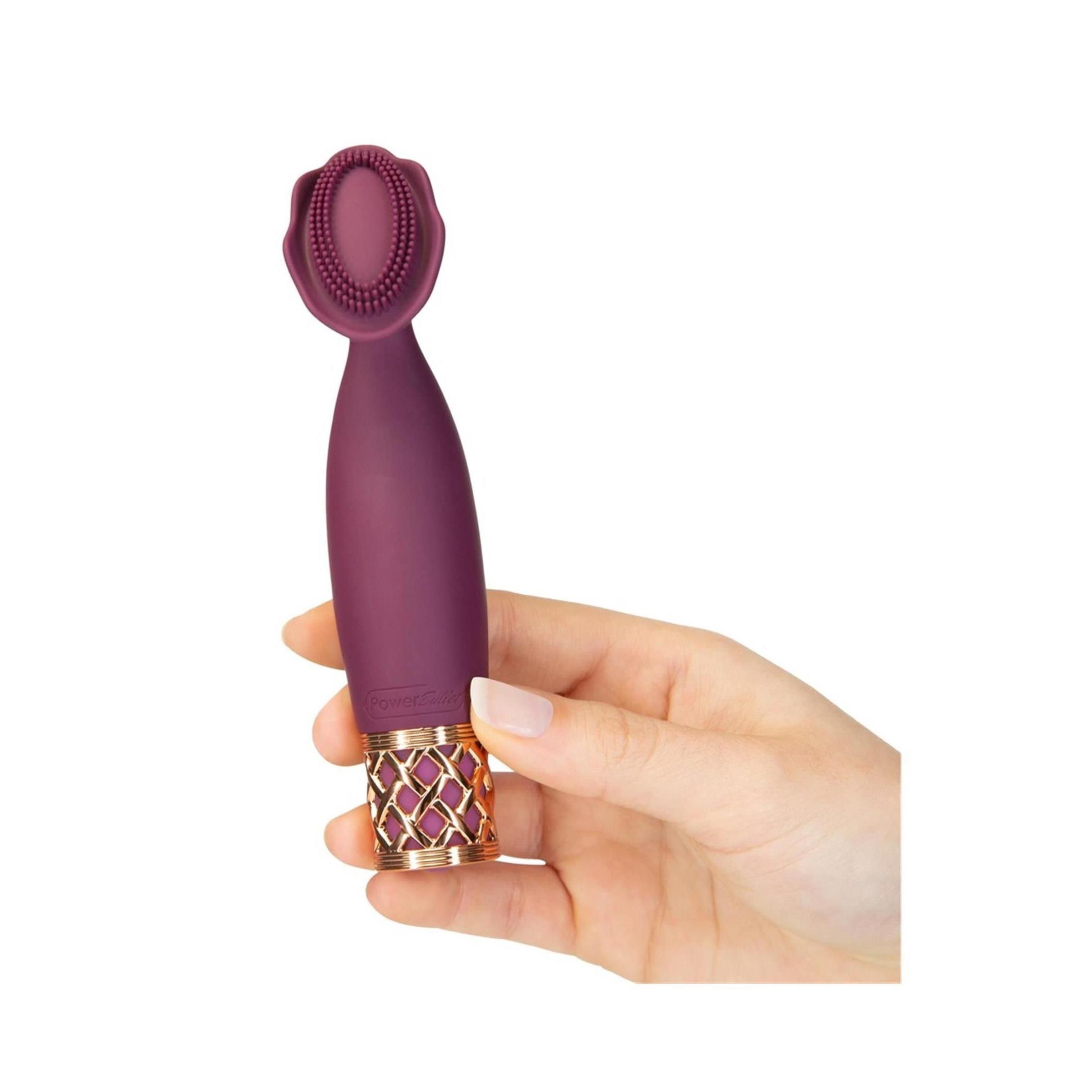 Hand hält lila Massagegerät. Goldfarbenes Gittermuster am Griff, blütenförmiger Aufsatz.
