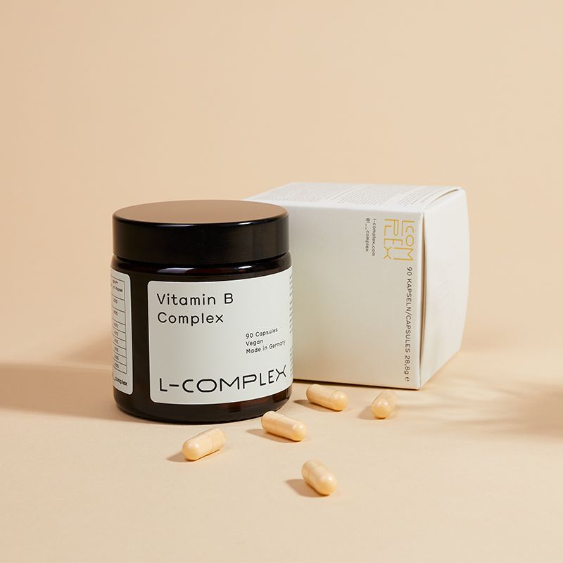 Braune Glasdose, weiße Schachtel und Kapseln. Dose mit "Vitamin B Complex", "90 Capsules", "Vegan", "L-COMPLEX".