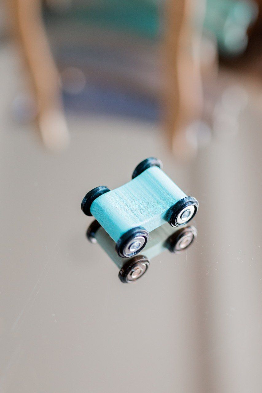 Kleines blaues Spielzeugauto mit schwarzen Rädern. Reflektiert auf einer glänzenden Oberfläche. Nahaufnahme.