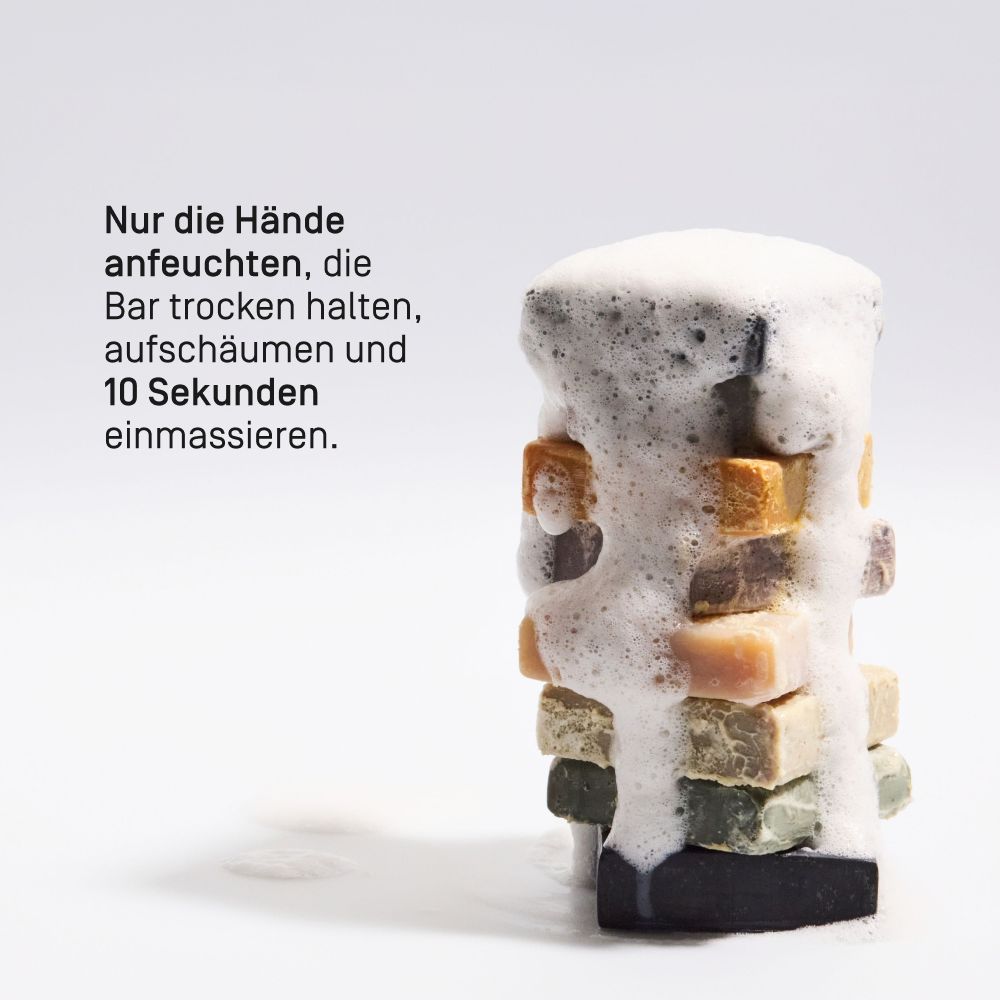 Gestapelte Seifenstücke mit Schaum. Anleitung: Hände anfeuchten, Bar trocken halten, aufschäumen, 10 Sekunden einmassieren.