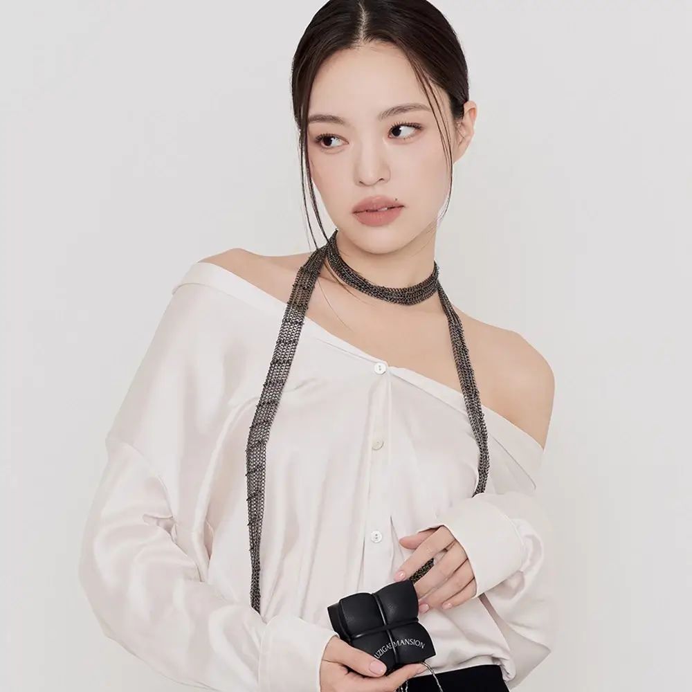 Frau mit weißem Oberteil und schwarzer Hose. Sie hält ein schwarzes, quadratisches Objekt in der Hand.