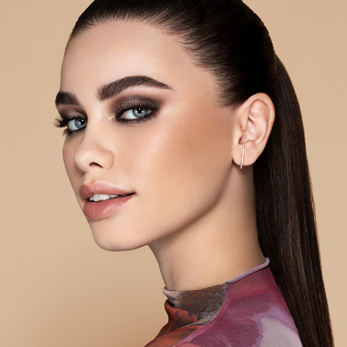 Porträt einer Frau mit dramatischem Smokey-Eye-Make-up, blauen Augen und einem dezenten Ohrring.
