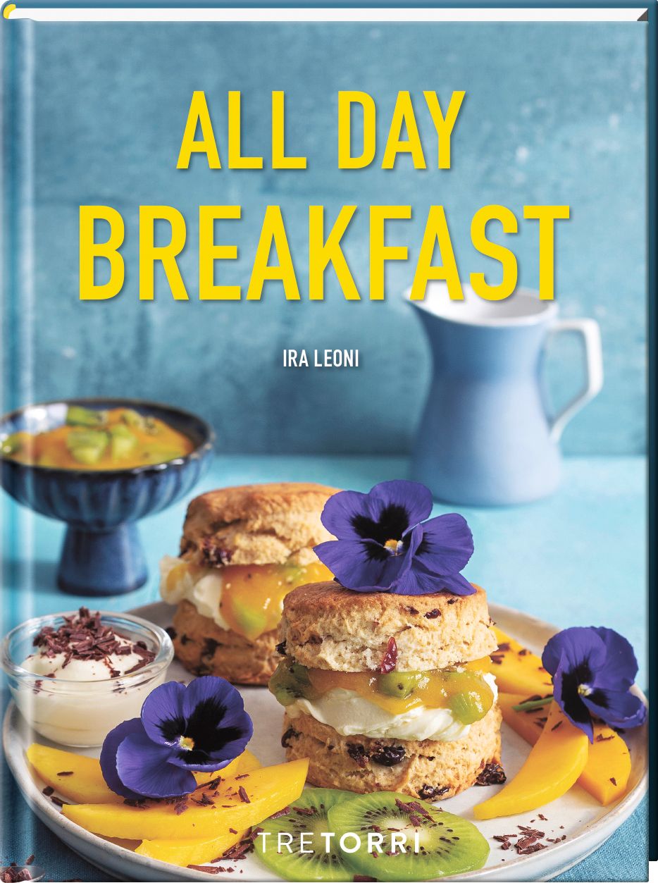 Buchcover mit Titel "All Day Breakfast" und Autor Ira Leoni. Auf dem Teller: Scones, Obst, Blüten. Blaue Kanne im Hintergrund.