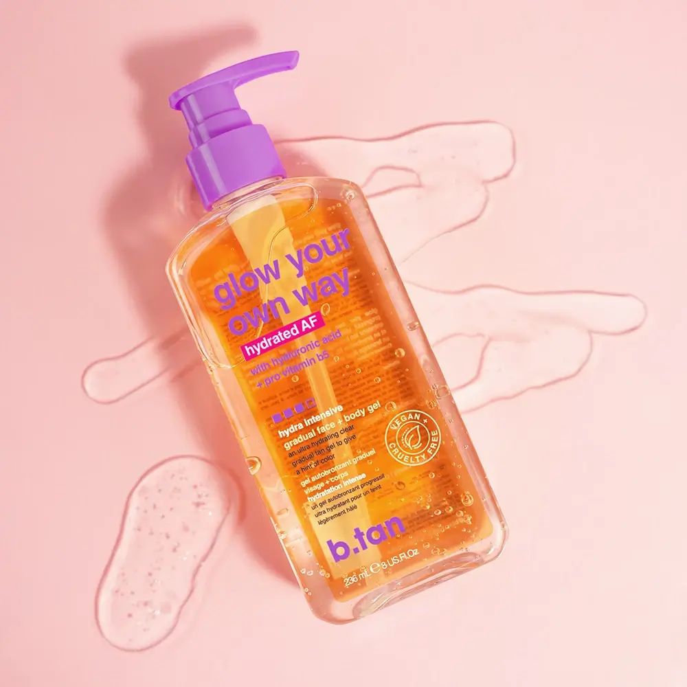 Transparente Flasche mit orangefarbenem Etikett. Aufschrift: glow your own way, hydrated AF, b.tan. Mit Pumpverschluss. Auf rosa Untergrund.