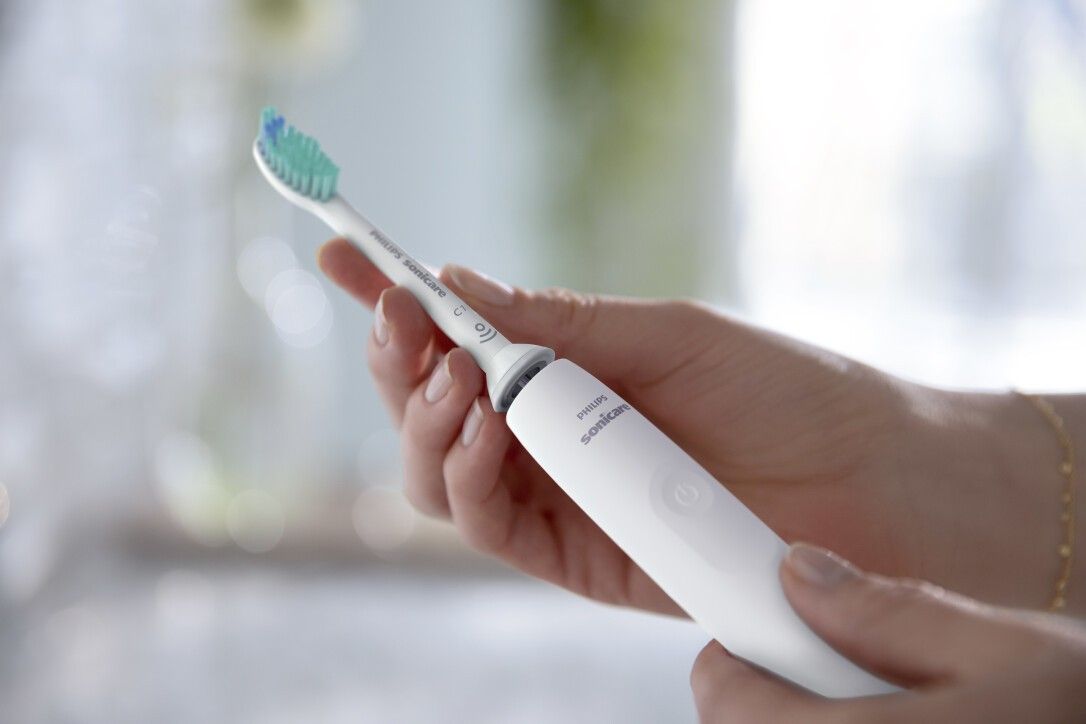 Weiße elektrische Zahnbürste in Händen gehalten. Bürstenkopf mit grünen Borsten. Philips Sonicare-Logo sichtbar.