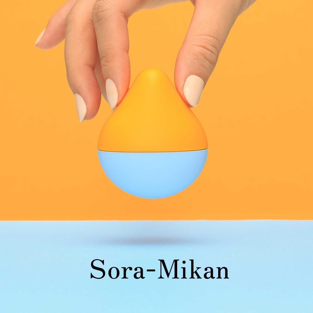 Produkt in Tropfenform, gehalten von einer Hand. Oberteil orange, Unterteil blau. Aufschrift: Sora-Mikan. Hintergrund: orange und blau.