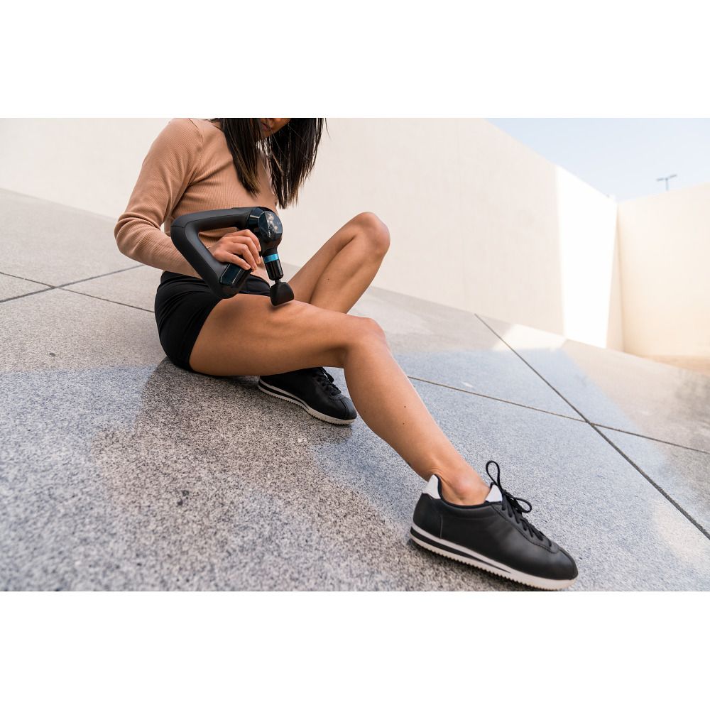 Person sitzt und verwendet ein schwarzes Massagegerät am Bein. Draußen.