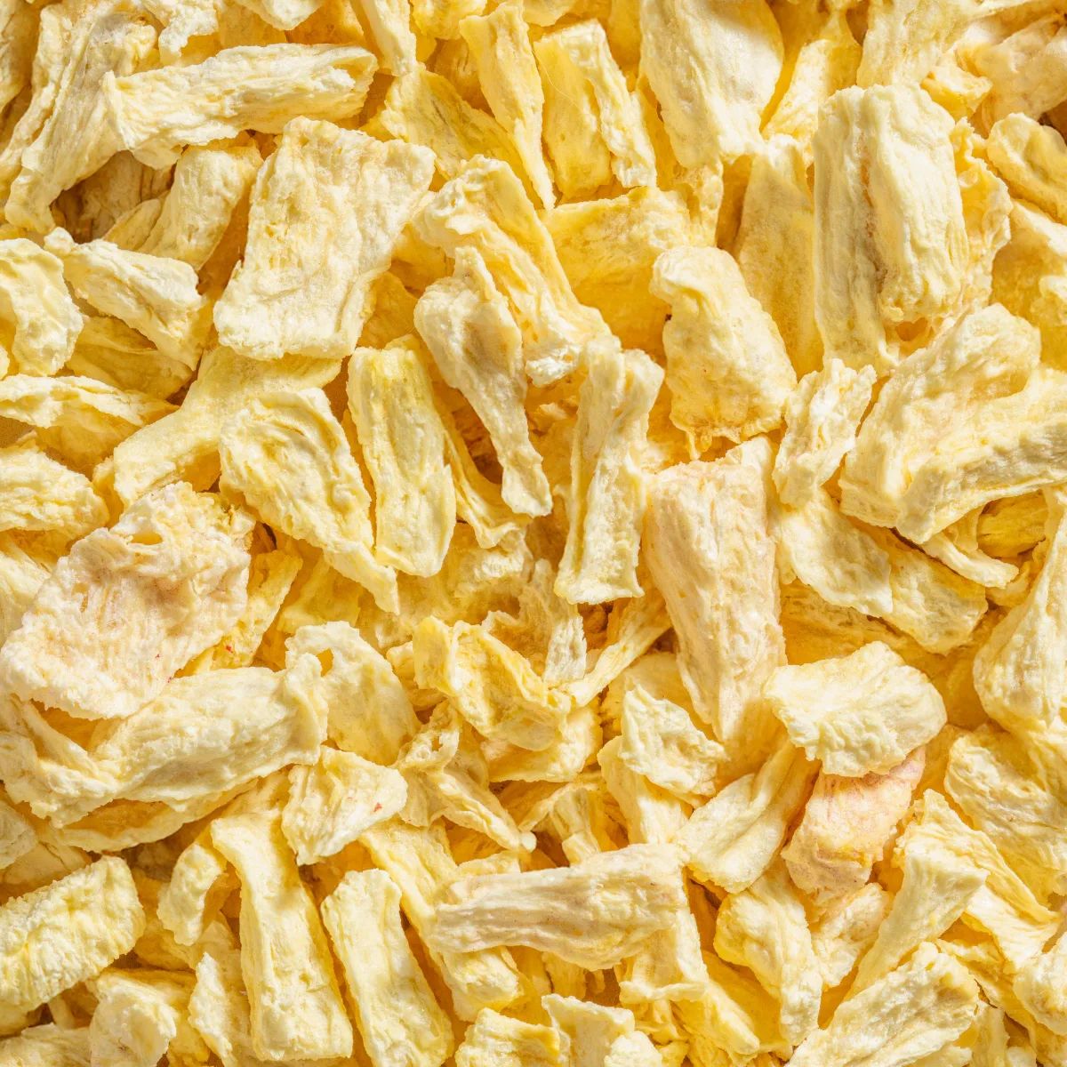 Nahaufnahme von gefriergetrockneten Ananas-Bits. Die Stücke sind hellgelb und unregelmäßig geformt.