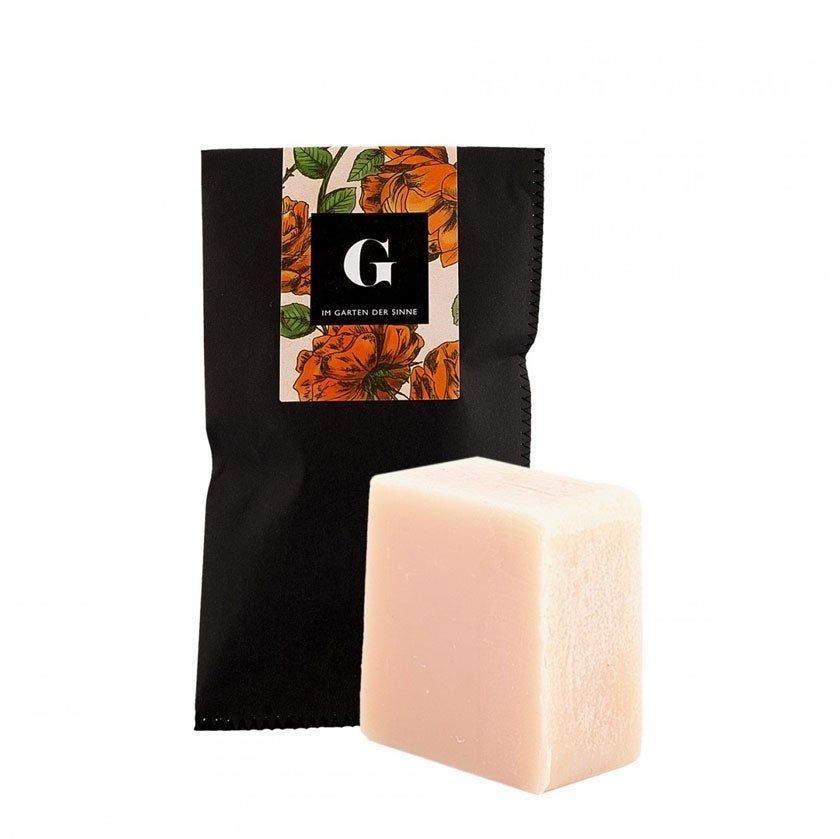 Rechteckige Seife neben schwarzer Verpackung mit floralem Muster und Logo "G".