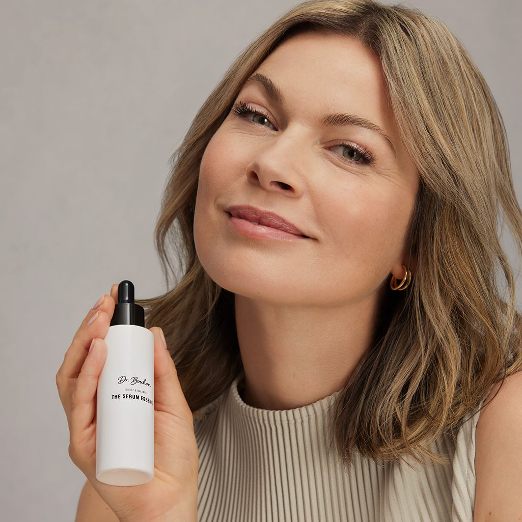 Femme tenant un flacon blanc avec bouchon noir. Inscription : Dr. Bouhon, THE SERUM ESSENCE.