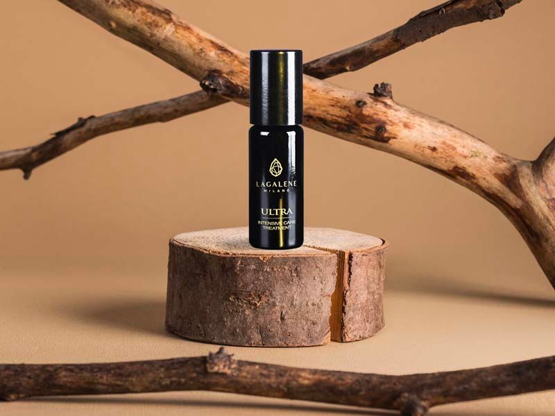 Eine schwarze Lagalene Milano Ultra Intensive Care Flasche steht auf einem Holzstück, umgeben von Ästen. Auf der Flasche steht "ULTRA INTENSIVE TREATMENT".