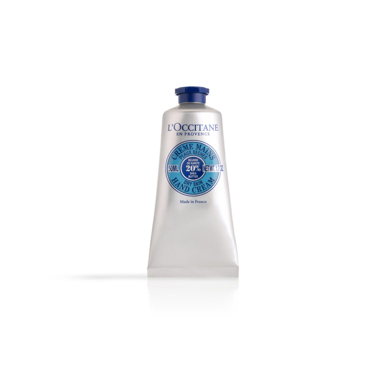 Creme-Tube. L'Occitane Handcreme. Blaue Kappe, silberner Tubenkörper. Aufschrift: Crème Mains, 20% Karité, Hand Cream.