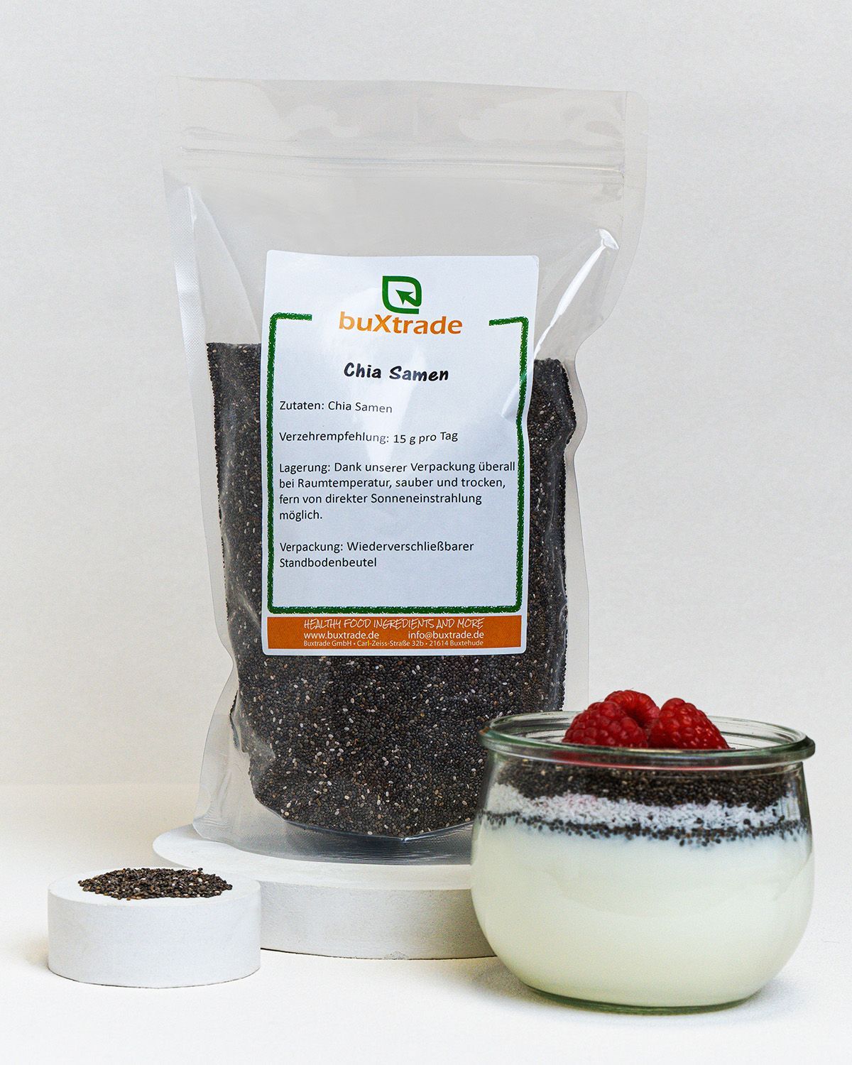 Verpackung mit Chia-Samen, Glas mit Joghurt, Himbeeren und Samen. Auf weißem Podest.